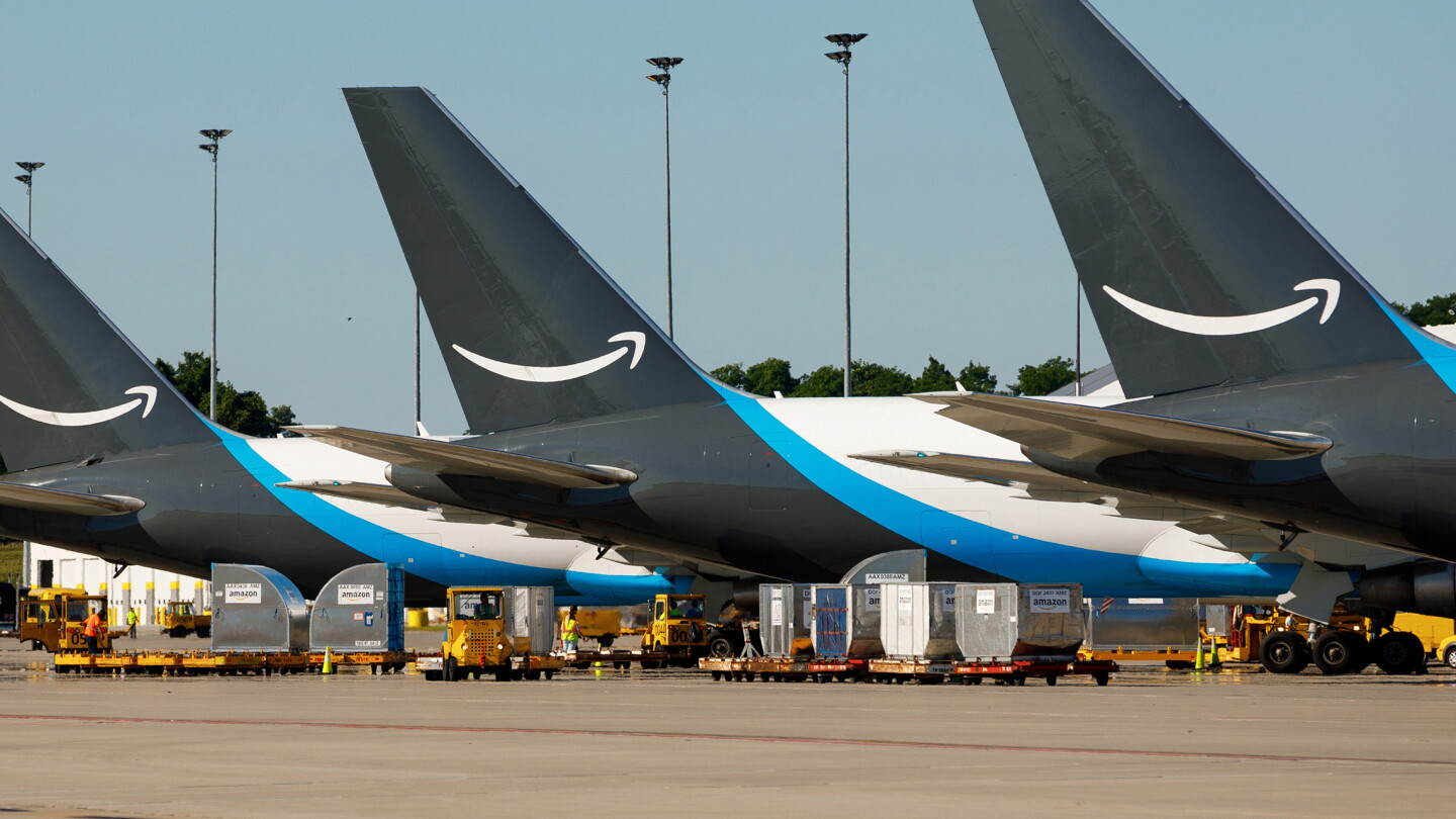 Three Amazon Air Boeing 767 cargo aircraft parked in a row on an airport tarmac, featuring dark tail fins with the white Amazon smile logo and blue fuselage accent stripes under a clear blue sky.